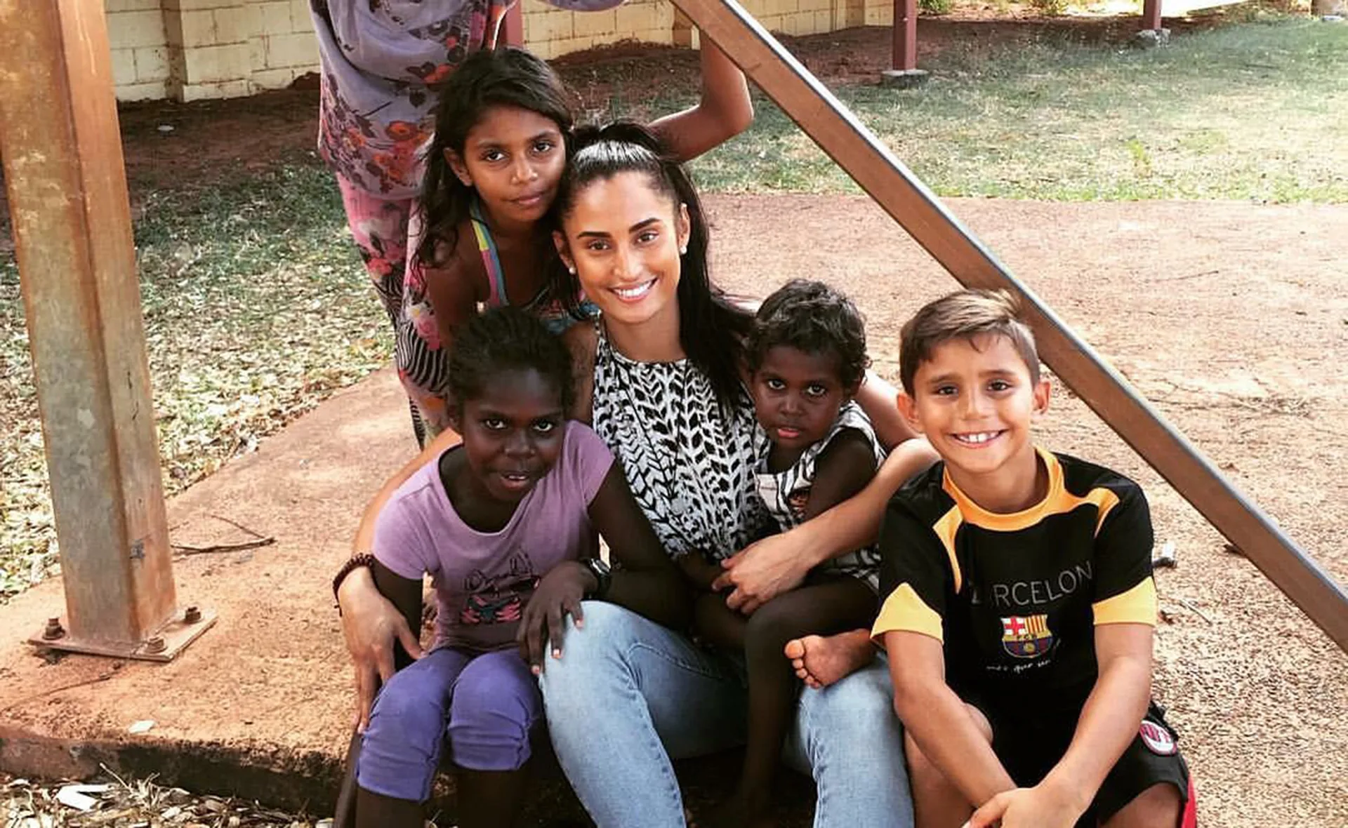 A woman smiles while sitting outdoors with four children, posing for a group photo on a sunny day.