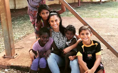 A woman smiles while sitting outdoors with four children, posing for a group photo on a sunny day.