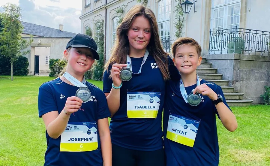Three children wearing "Royal Run" shirts, each holding a medal and smiling in front of a building.