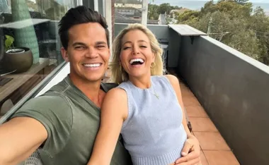 A couple smiling together on a balcony, embracing each other with a scenic view in the background.