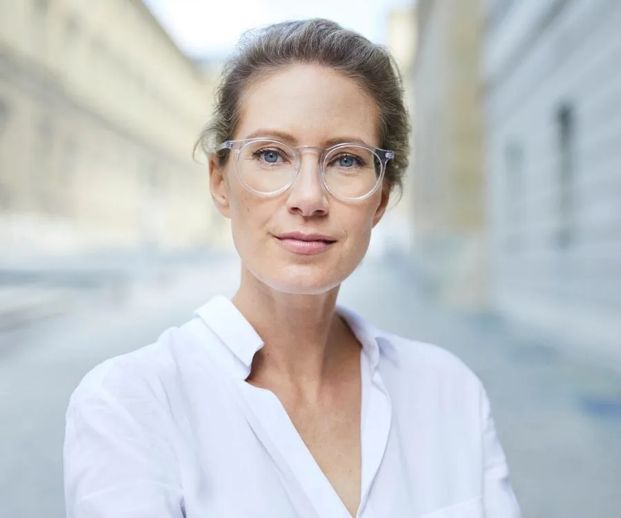 Middle-aged woman with glasses, standing on a street, looking confident.