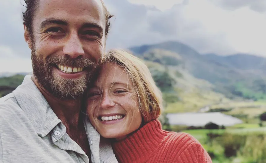 Couple smiling outdoors with mountains in background.