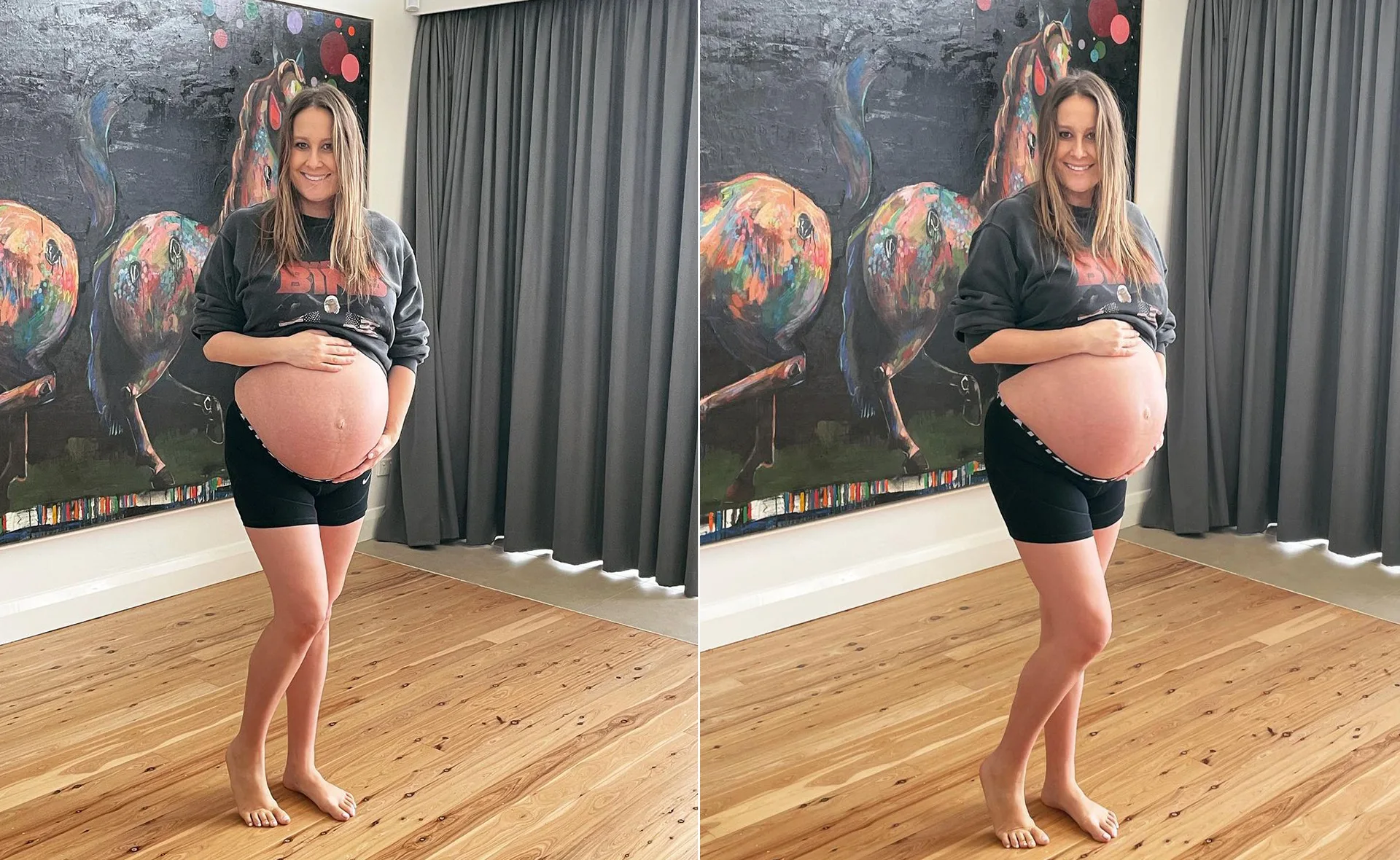 A pregnant woman smiling, holding her belly, standing barefoot in front of a colorful art piece.