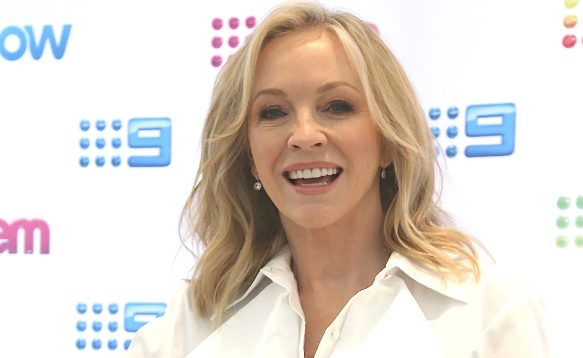 Blonde woman smiling in front of a media wall with colorful logos.