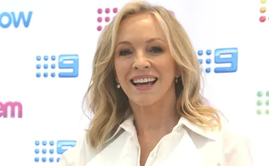 Blonde woman smiling in front of a media wall with colorful logos.