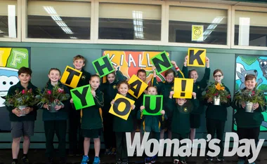 Children holding "THANK YOU!" signs and flowers, smiling at the camera in front of a green wall, "Woman's Day" logo visible.