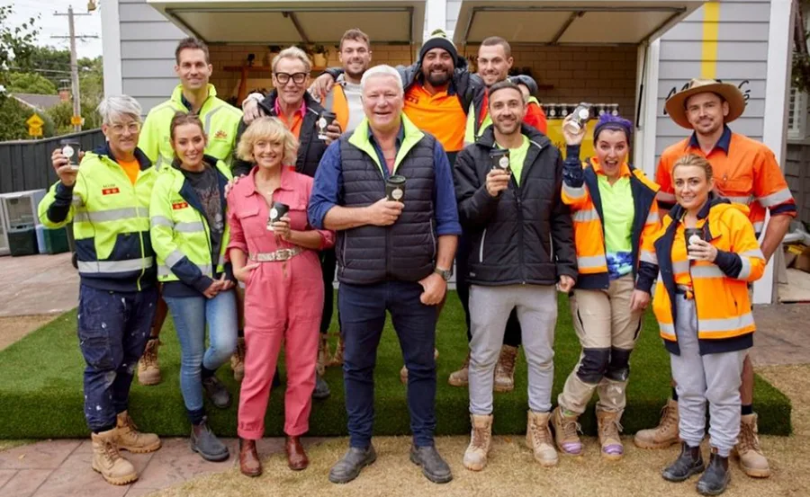 Group of people outside a garage, holding coffee cups, wearing safety and casual clothing, smiling at the camera.