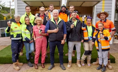 Group of people outside a garage, holding coffee cups, wearing safety and casual clothing, smiling at the camera.