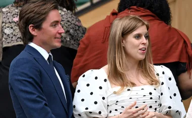 Man in a blue suit with a polka dot tie, standing next to a woman in a white dress with black polka dots, talking.