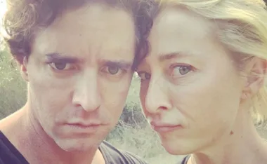 A couple taking a selfie outdoors with neutral expressions.