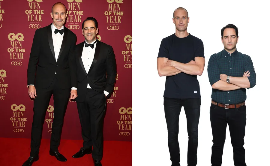Two men posing together; one in a tuxedo, the other in casual wear; GQ Men of the Year event backdrop.