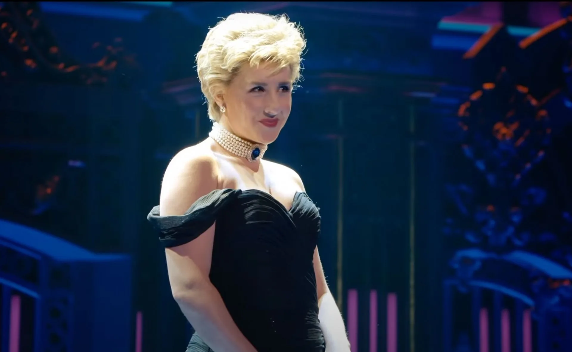 Actress in a black dress and pearl choker, performing on stage in the Princess Diana musical.