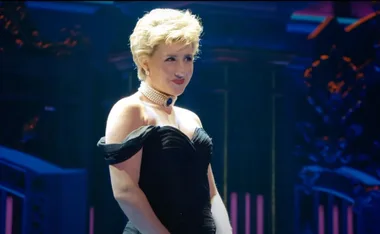 Actress in a black dress and pearl choker, performing on stage in the Princess Diana musical.