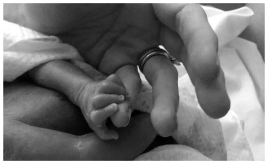 An adult hand gently holds a newborn's tiny feet, symbolizing care and tenderness.