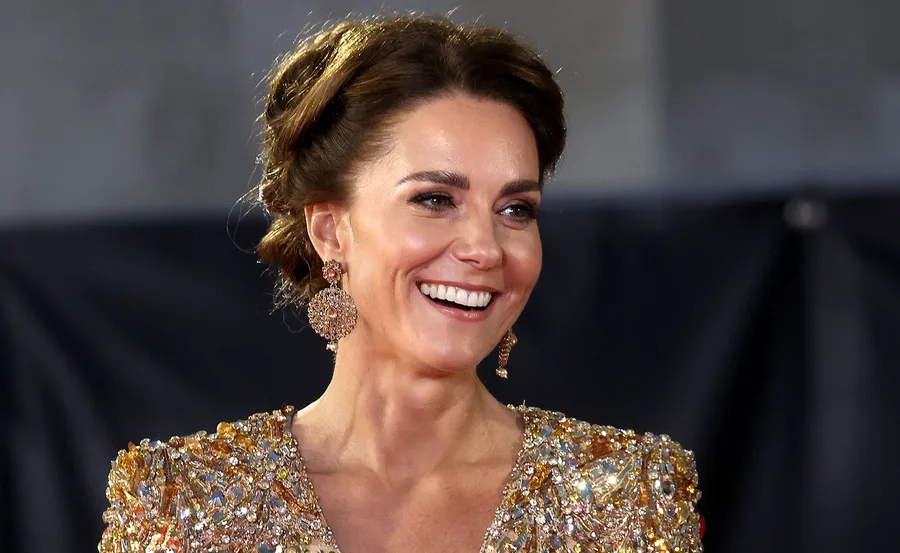 Woman smiling in a sparkling gold dress with intricate detailing and matching earrings at a formal event.