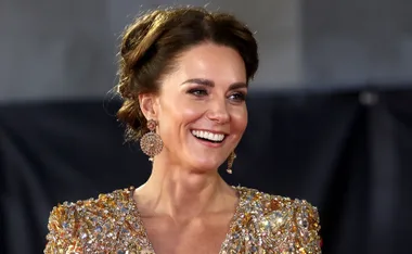 Woman smiling in a sparkling gold dress with intricate detailing and matching earrings at a formal event.