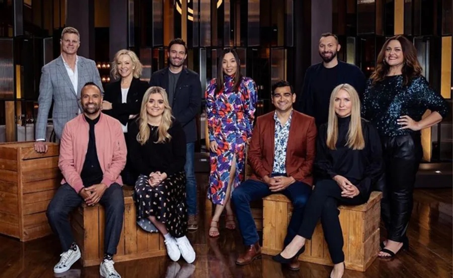 Group photo of "MasterChef Australia 2021" judges and contestants on a wooden stage, smiling at the camera.