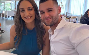 A smiling couple seated at a dining setting, with bright windows in the background.