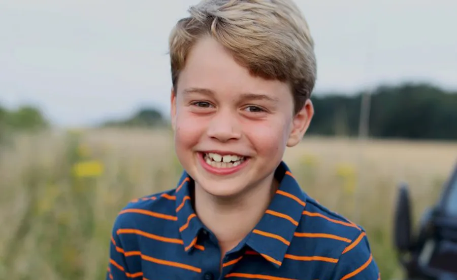 Young boy smiling outdoors, wearing a striped shirt, with a blurred nature background.