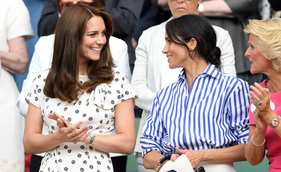 Two women smiling and talking while standing among a crowd at a public event.