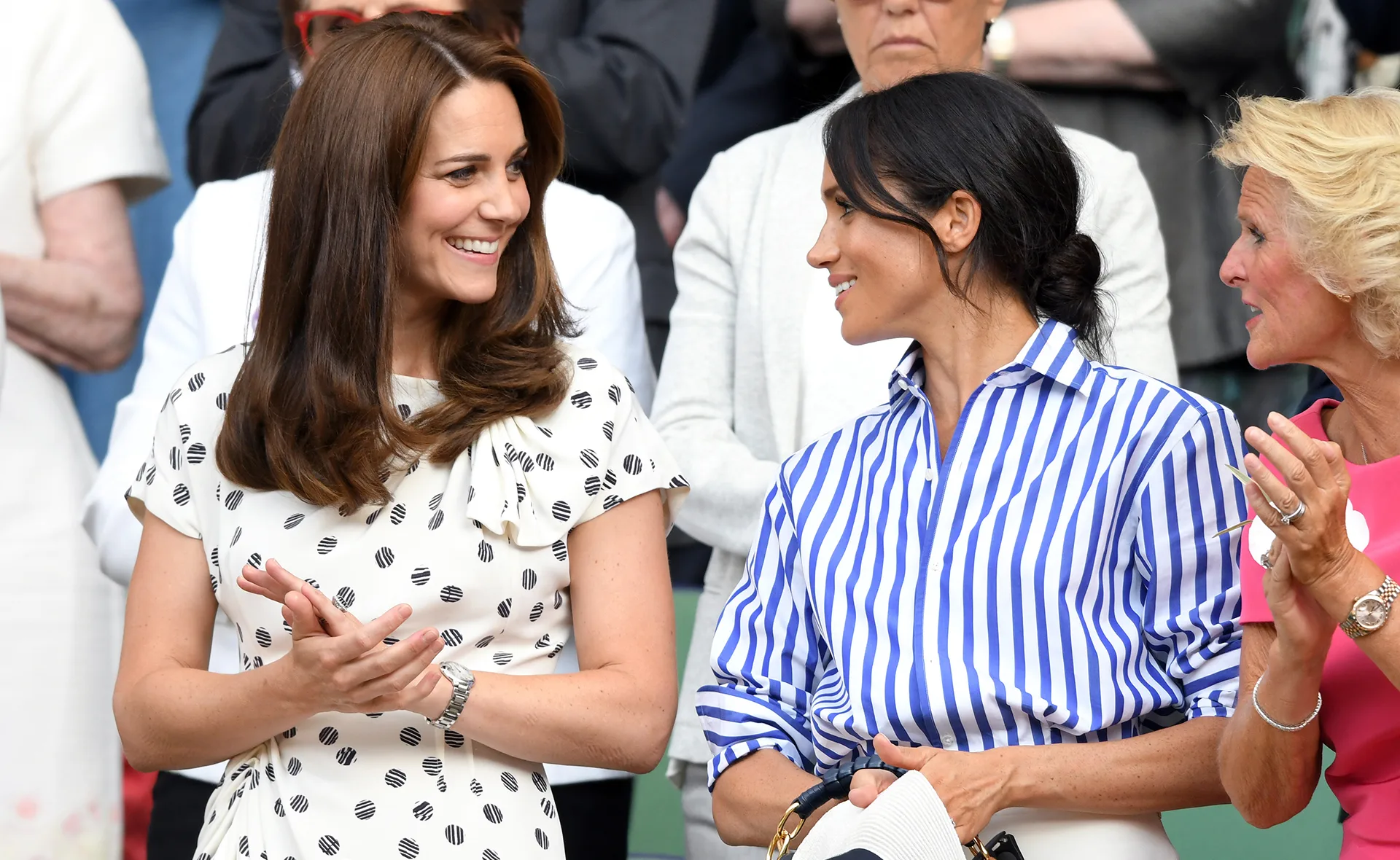 Two women smiling and talking while standing among a crowd at a public event.