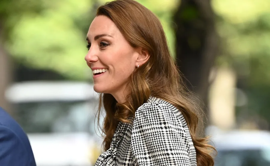A woman with long brown hair smiles, wearing a black and white houndstooth dress, outdoors.