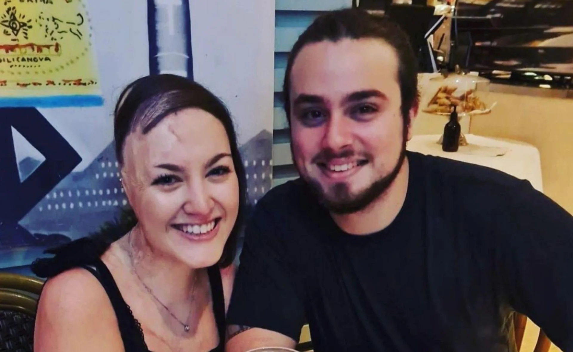 A smiling couple in a cozy indoor setting, with colorful artwork in the background.