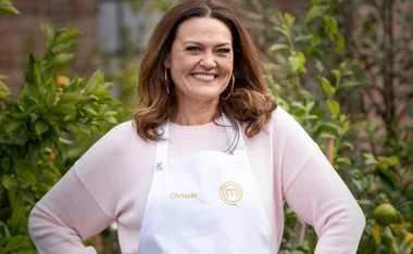 Chrissie Swan smiling in a "MasterChef" apron outdoors, surrounded by greenery.