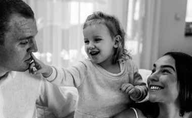 A happy family moment with a child playfully touching an adult's nose, while another adult smiles, all in black and white.