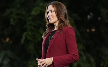 Princess Mary wearing a red blazer, standing outdoors with greenery in the background.