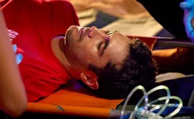 A man in a red shirt lies on a stretcher during an emergency, with medical equipment around him.