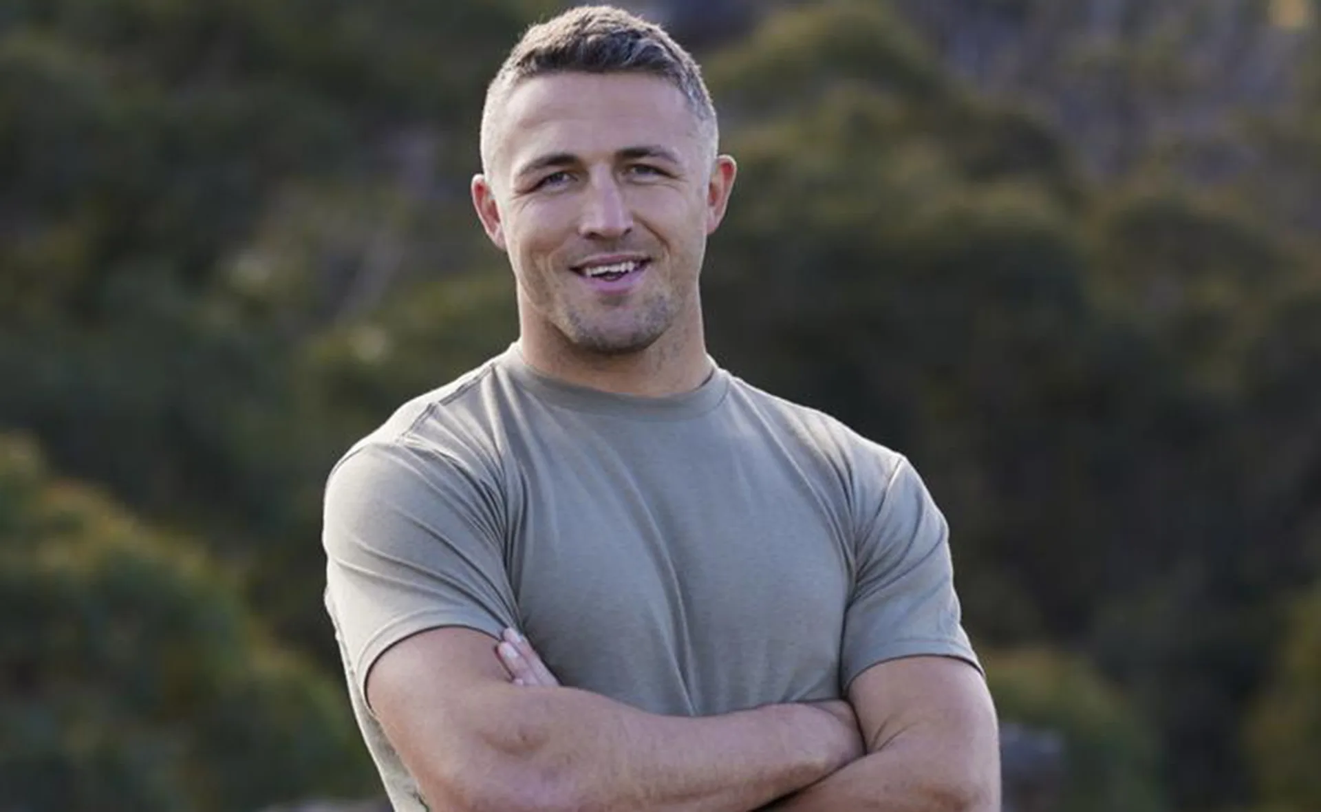 Man in a green shirt smiling with arms crossed, outdoors.