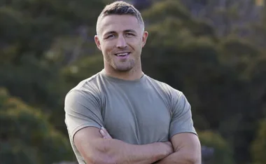 Man in a green shirt smiling with arms crossed, outdoors.