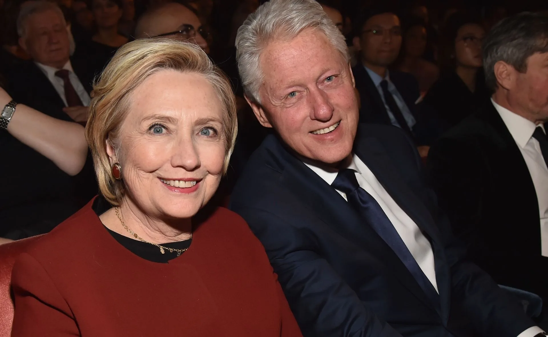 Two people smiling at an event, one wearing a red top, and the other in a dark suit and tie.