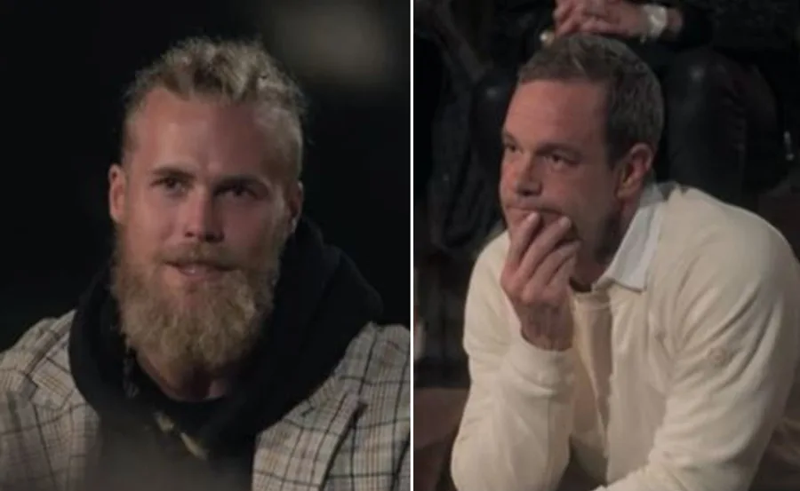 Two men seated, one with a beard and plaid jacket, the other in a light sweater, appear thoughtful during a conversation.