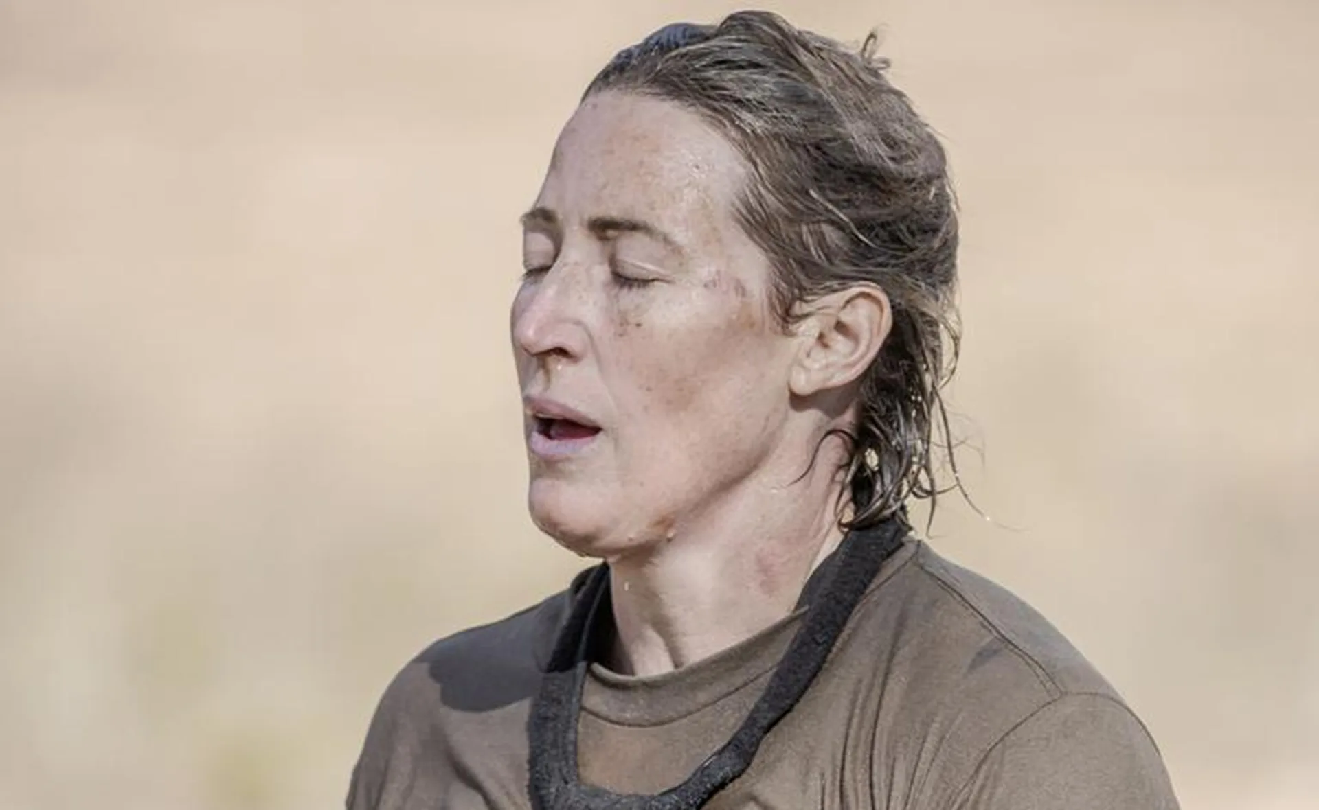 Woman with closed eyes, wearing a brown shirt, looking exhausted, outdoors.