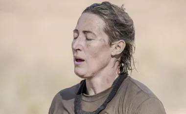Woman with closed eyes, wearing a brown shirt, looking exhausted, outdoors.