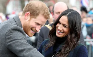 Prince Harry and Meghan Markle laughing together at an outdoor event.