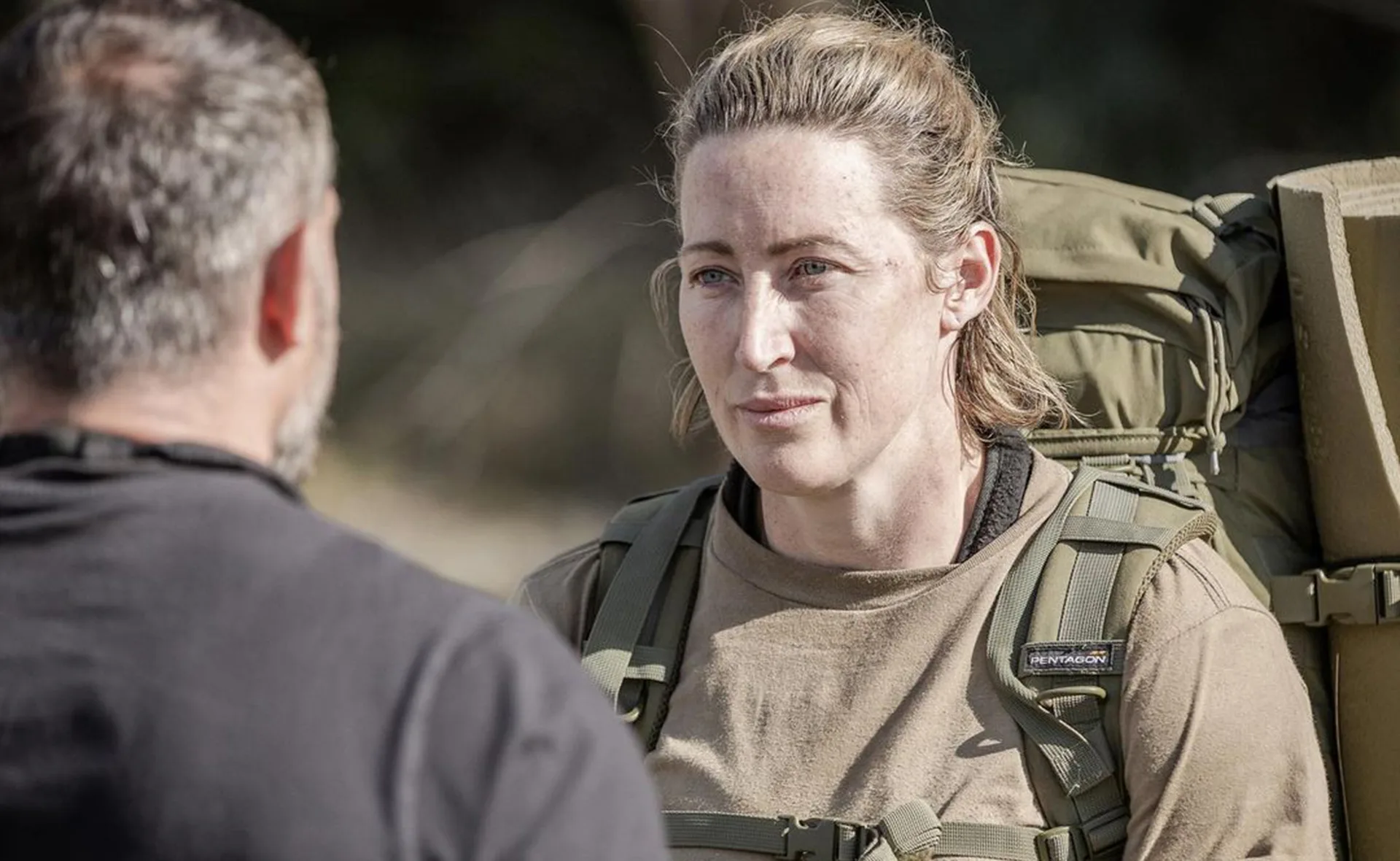 A woman in military-style gear listens intently to a man outdoors.
