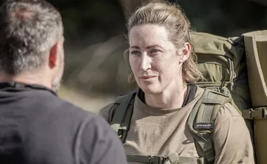 A woman in military-style gear listens intently to a man outdoors.