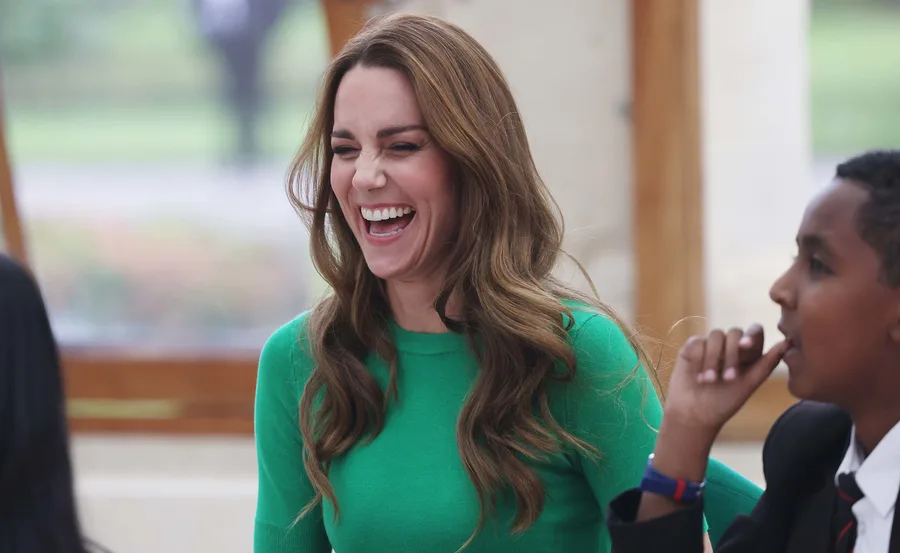 A woman in a green coat smiling broadly in a social setting.