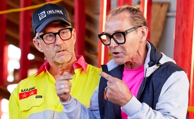 Two men in discussion, one in a construction uniform and hat, the other in casual wear, both wearing glasses.