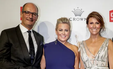 Three people smiling at an event, dressed in formal evening attire, against a branded backdrop.