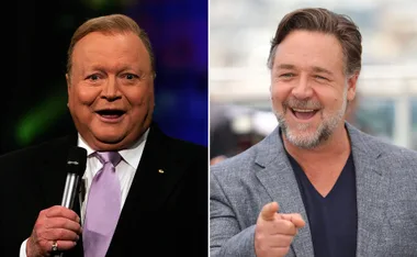 Two men smiling side by side; one is holding a microphone, the other pointing. They are in a biopic discussion.