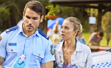 Police officer and woman in casual wear outdoors, discussing something with serious expressions.