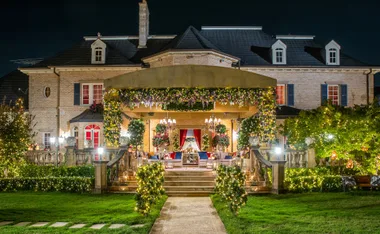A grand house at night, adorned with vibrant lights and floral decorations, set for a festive or romantic gathering.