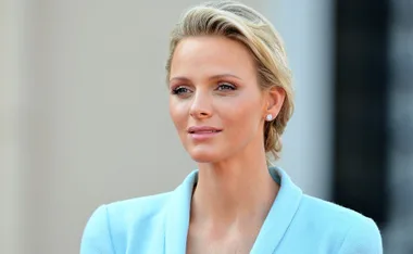 A woman with short blonde hair wearing a light blue outfit and stud earrings, looking into the distance.