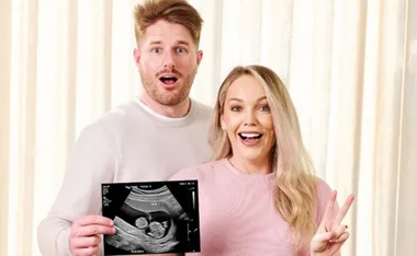 Couple smiling while holding ultrasound image, announcing pregnancy.