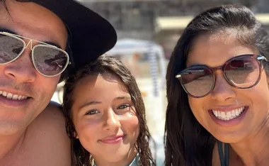 Three people smiling, wearing sunglasses at the beach on a sunny day.