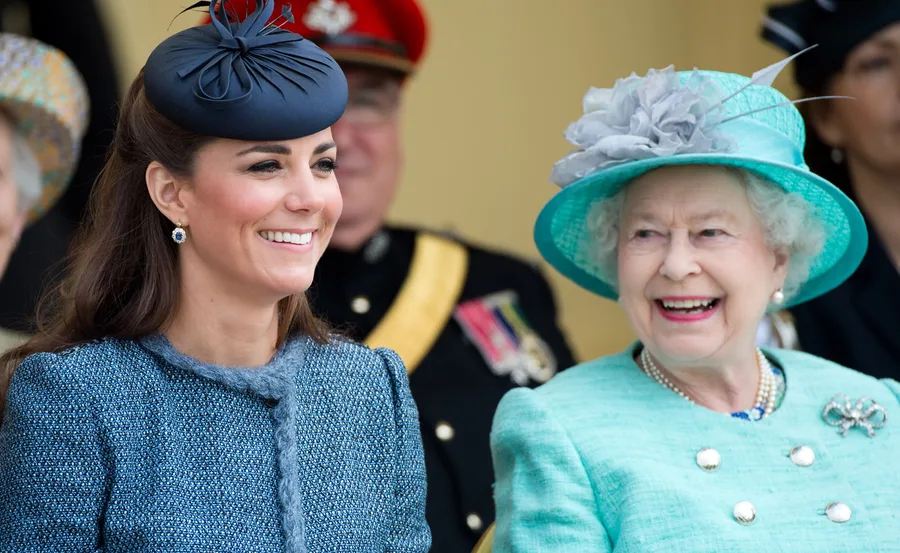 Two women smiling at a public event, both wearing hats and formal attire.
